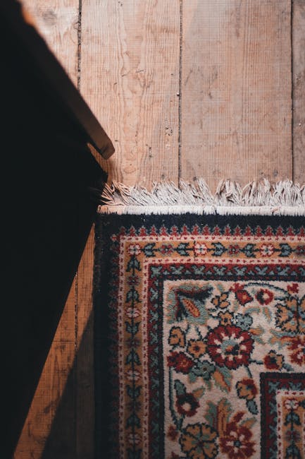 A pile of old carpets with ornate patterns and fringed edges, leaning against a wall on a city sidewalk. The carpets appear worn and partially rolled, with some sections folded or crumpled. Surrounding the carpets are large white and beige sacks filled with debris, possibly from a disposal or renovation process. Wooden planks and pieces of discarded construction material are scattered on the ground nearby, which is paved with concrete tiles. The scene is outdoors, with natural daylight illuminating the area. The setting suggests a residential or commercial space undergoing cleaning, renovation, or carpet disposal, with no visible cleaning tools or products present. Carpet Cleaning Marylebone offers surface and deep cleaning services, including responsible disposal of old carpets, ensuring hygienic and well-maintained environments.